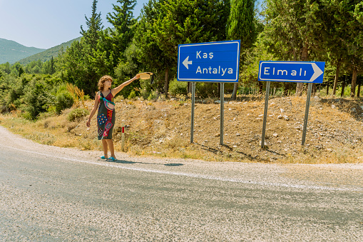 A woman hitchhiking in front of the Antalya Kas sign