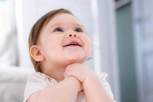 Excited cute little baby girl thinking of something dreaming or having a good idea, smiling and looking up, imagination. stock photo
