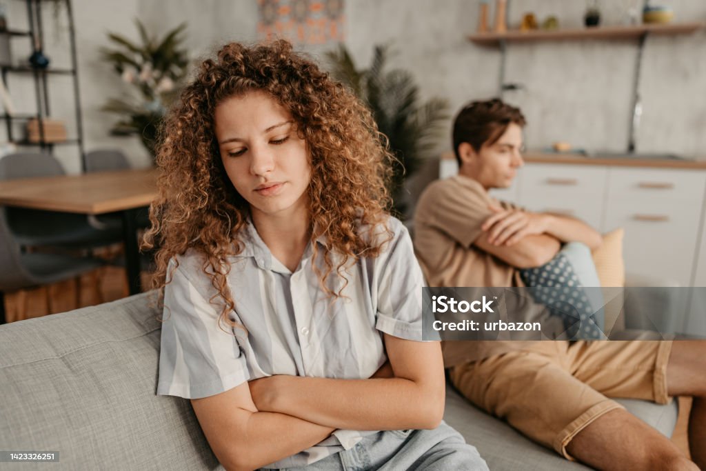 Young Couple Arguing At Home Young couple with relationship problems, sitting on the sofa in the living room and arguing. Young Couple Stock Photo