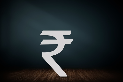 Rupee symbol on a dark blue screen with wooden table background, investment, banking and finance concept