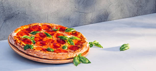 Pepperoni pizza with basil on kitchen table in sunlight stock photo