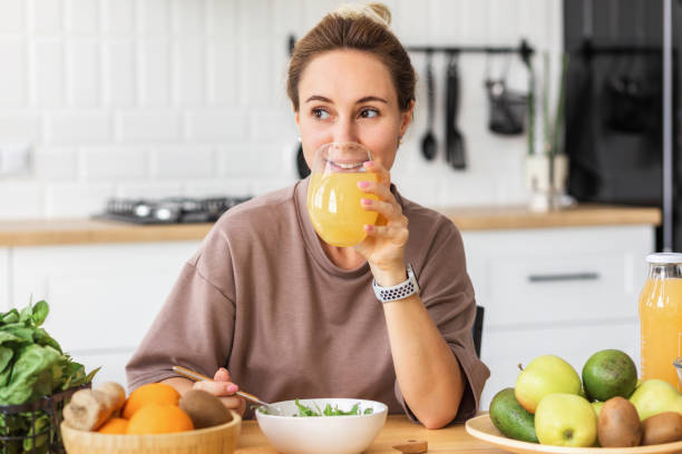 healthy lifestyle. Happy young woman eating salad and drinking orange juice while sitting at home in the kitchen. Young female eat wholesome breakfast stock photo