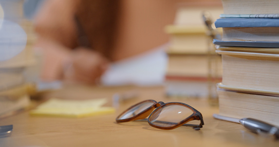 Glasses, books and post it note of learning, studying and education tools of a student and mockup. Book and writing tool with a female writing in the blur background and mock up preparing for a test