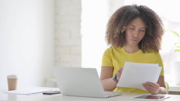 istock African Woman with Laptop Reading Documents in Office 1423335314