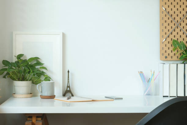 istock Comfortable workplace with empty picture frame, coffee cup, books and hours plant. 1423337471