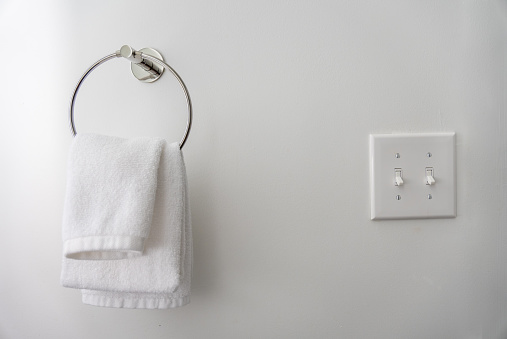 White hand towel and light switch with white wall.
