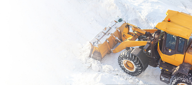 A large orange tractor removes snow from the road and clears the sidewalk. Cleaning and clearing roads in the city from snow in winter. Snow removal after snowfalls and blizzards.