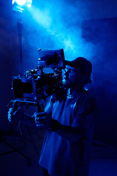 istock Serious young cameraman with steadicam standing against spotlight 1423343389