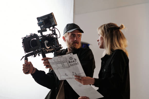 istock Young bearded cameraman and his assistant consulting about shooting 1423343395