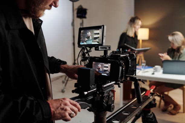 istock Young man with videocamera standing in studio in front of two women 1423343419