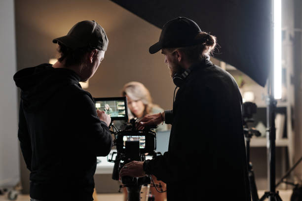 Back view of two young men standing in front of camer aand using steadicam Back view of two young men standing in front of camer aand using steadicam while shooting new commercial with female model behind the scenes stock pictures, royalty-free photos & images