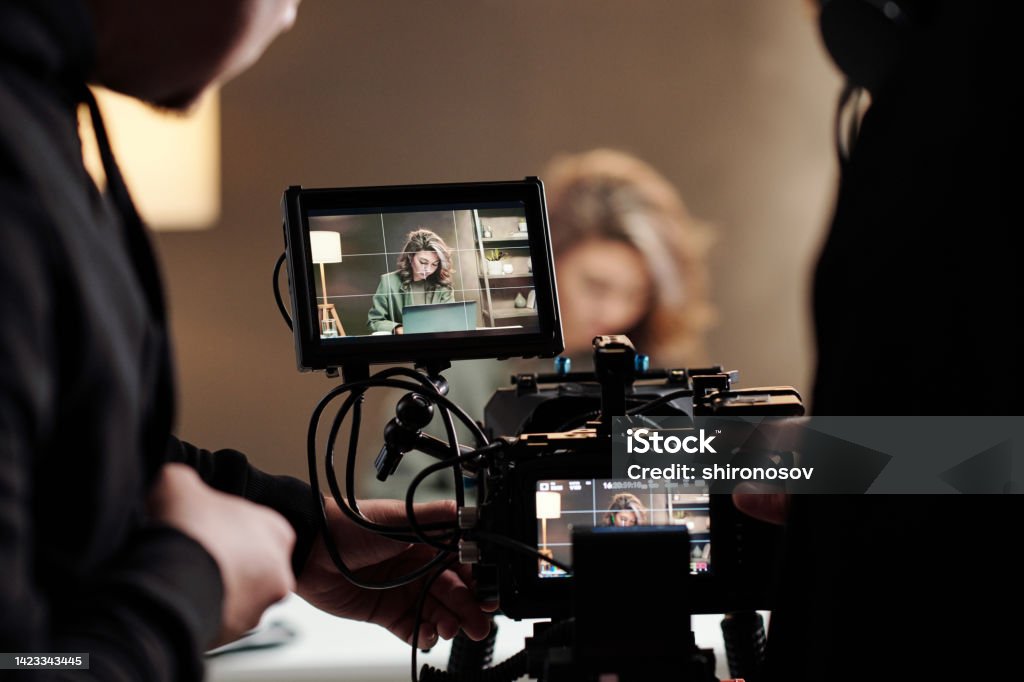Close-up of steadicam screens with female model using laptop by table Close-up of steadicam screens with female model using laptop by table during commercial being shot by cameraman and his assistant Filming Stock Photo