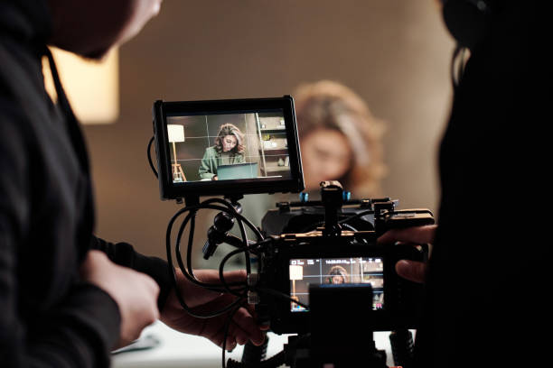 Close-up of steadicam screens with female model using laptop by table Close-up of steadicam screens with female model using laptop by table during commercial being shot by cameraman and his assistant film crew stock pictures, royalty-free photos & images