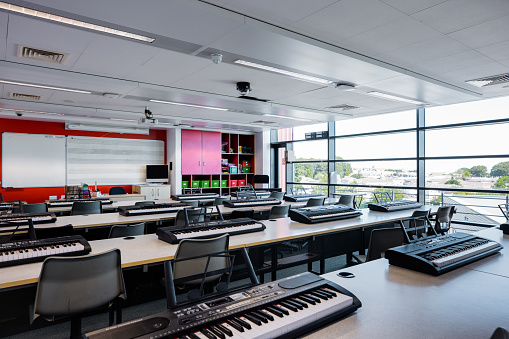 A music classroom filled with desks and chairs in a secondary school in the North East of England. There are electric keyboards on each desk.