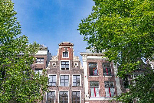 Amsterdam canal house facades with a blue sky in the background during summer.