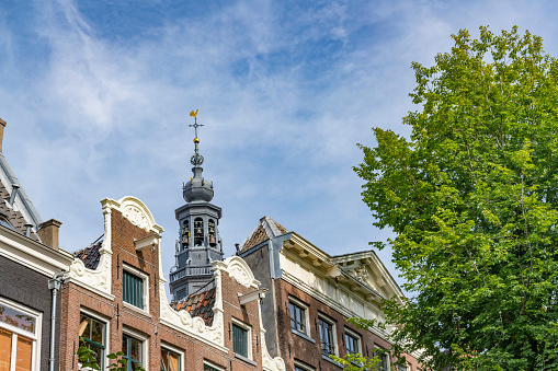 Amsterdam canal house facades with the Zuiderkerk church tower and a blue sky in the background during summer.