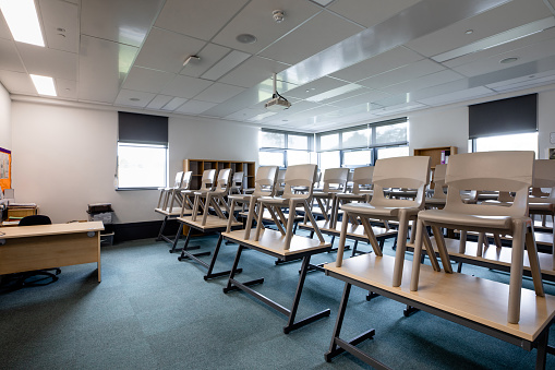 A classroom filled with desks and chairs in a secondary school in the North East of England. The chairs are up on the desks.