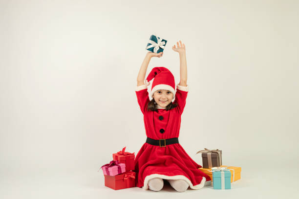 Little Girl in Santa Costume Little girl in santa costume is sitting on white background with Christmas presents. elf sitting stock pictures, royalty-free photos & images