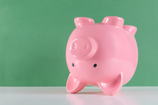 Piggy bank upside down on white table in front of green background.