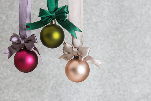 Three pink and golden colored christmas baubles hanging with shiny ropes.
