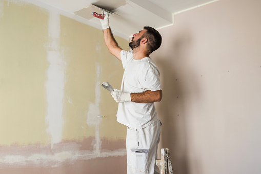 Young man in white uniform painting ceiling
