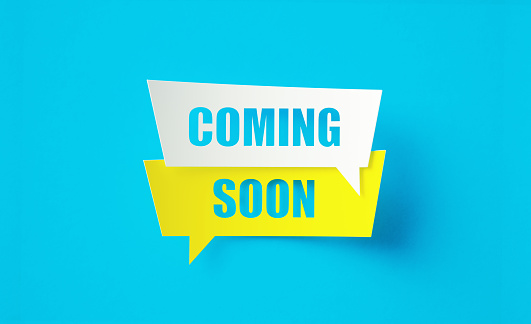 Coming soon written cut out yellow and white speech bubbles sitting on blue background. Horizontal composition with copy space.