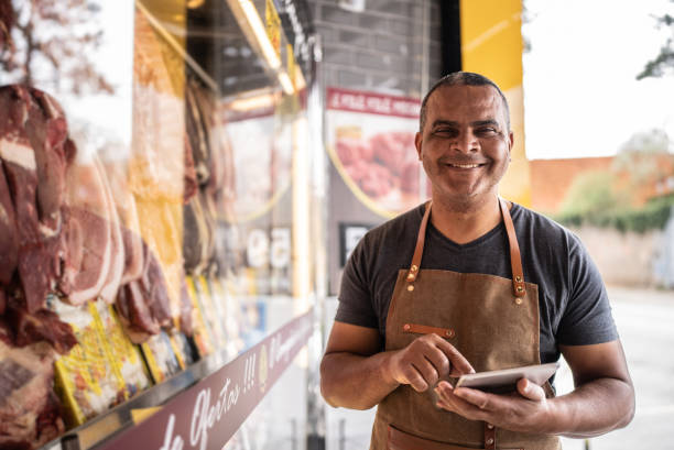 portrait of a butcher's shop owner using digital tablet - supermarket meat store manager imagens e fotografias de stock