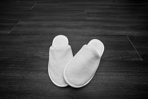 pair soft white slippers on wooden floor, monochrome