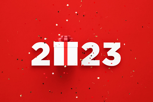 2023 and white gift box sitting behind gold colored confetti over red background. Horizontal composition with copy space. Directly above. Great use for Christmas concepts.