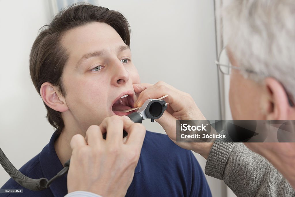 Throat Exam With Depressor Young man getting his throat checked by male doctor at clinic Uvula Stock Photo