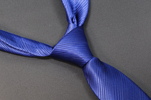 Blue tie with a classic knot on a gray background.