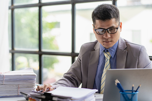 Young Asian businessman working with piles of papers on the desk of financial business ideas.