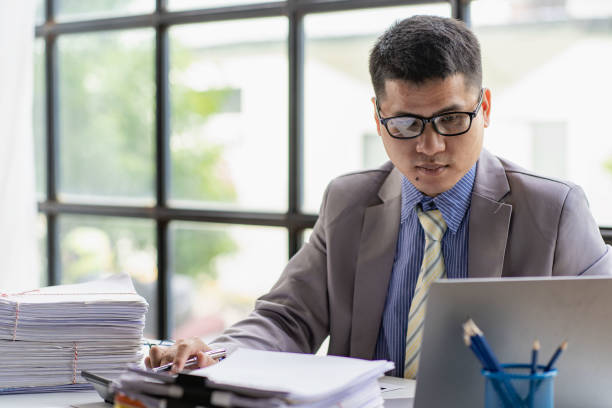 Young Asian businessman working with piles of papers on the desk of financial business ideas. stock photo