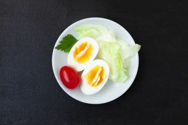 Halves of hard boiled chicken egg with lettuce and tomato on a plate - top view