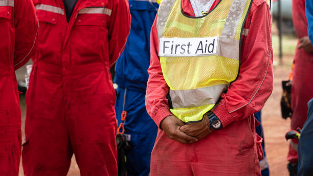 First Aid person in emergency drill. Group meeting of field operation staffs with a man who wear "First Aid" vest, preparing for emergency drill and practice scenario at construction site. Industrial people working scene photo. drill team stock pictures, royalty-free photos & images