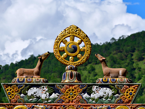 Punakha, Bhutan: Punakha Dzong, aka Pungtang Dechen Photrang Dzong - Dharma wheel atop the entrance gate - the eight spokes represent the Noble Eightfold Path of Buddhism. Buddhists believe that the first turning of the wheel occurred when the Buddha taught the five ascetics at the Deer Park in Sarnath, because of this, dharmachakras are often represented with a deer on each side - the base includes two Snow Lions, a Bhutanese and Tibetan symbol (part of the flag of Tibet), representing power and strength, fearlessness and joy, east and the earth element - Vajrayana Buddhism.
