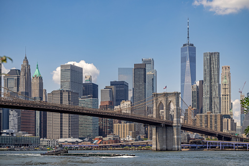 DUMBO, Brooklyn, New York, NY, USA - July 14th 2022:  View towards the south Manhattan skyline with the Brooklyn Bridge in front and with a barge on East River