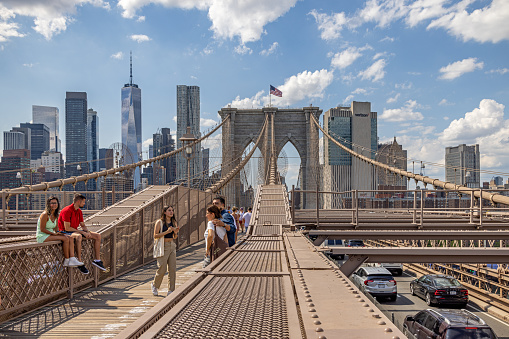 Brooklyn Bridge, New York, NY, USA - July 14th 2022:  People walking on a old suspension bridge, the Manhattan Bridge with a view to the urban skyline on South Manhattan