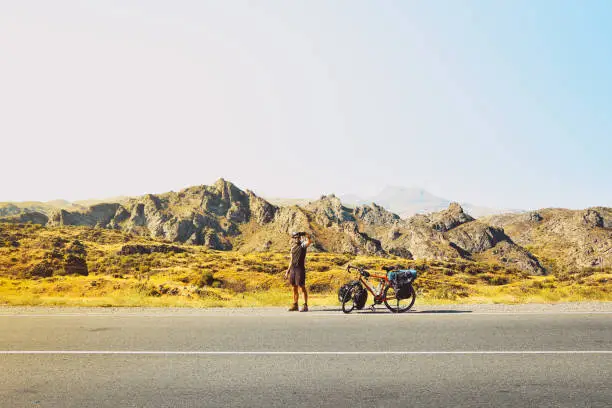 Photo of Cinematic travel inspirational panorama caucasian traveler cyclist stand on road take smiley self-portrait with mobile phone. Solo travel bicycle touring around the world