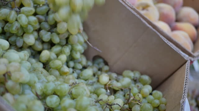 the hand of an older adult woman takes bunches of grapes in a box in the market to buy and eat fruits, natural and organic, useful for the old human body.