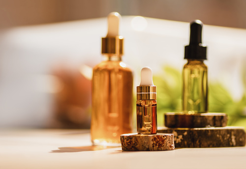Cosmetic glass dropper bottles on wooden podium with oil, serum, fruit peeling in the sunlight. Soft focus. Natural beauty products background. Morning routine, skin care concept. Front view, mockup