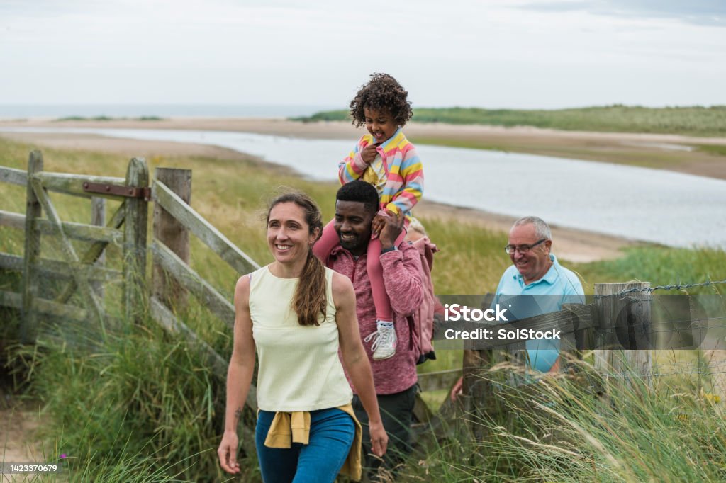 Lets Head Into The Dunes A medium front view of a mother who is leading her family along a coastal trail of sand dunes in Beadnell bay in the North East of England. They are all on a family staycation and enjoying a getaway near the beach together as a family. Coastline Stock Photo