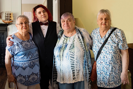 Red hair future bride family portrait with mother, aunt and grandmother before LGBTQ+ wedding. She is one of the brides, and this is part of a series about a lesbian couple getting married. Horizontal indoors waist up shot with copy space.