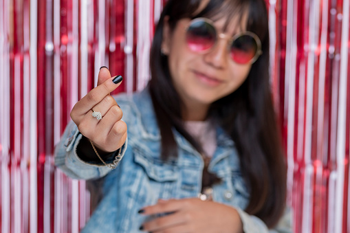 Teenager at party with glasses making korean heart sign with fingers.