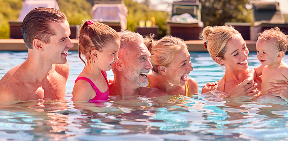 Smiling Multi-Generation Family With Baby Boy On Summer Holiday Relaxing In Swimming Pool