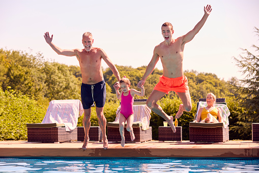 Multi-Generation Family On Summer Holiday Jumping Into Swimming Pool