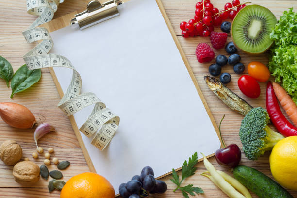 istock Fresh fruits and vegetables, nuts, fish, legumes and empty notebook with measuring tape on wooden background, top view. Healthy food and balanced diet concept 1423372109