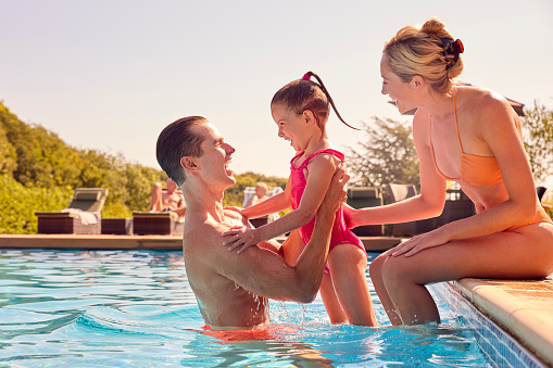 Smiling Family On Summer Holiday Playing In Swimming Pool
