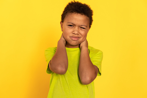 Portrait of displeased preteen boy rubbing neck. Mixed race child wearing green T-shirt suffering from neck ache. Childs health problems concept