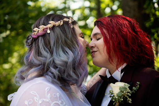Portrait of newlywed brides kissing outdoors in summer. This is part of a series about a lesbian couple getting married. Horizontal outdoors waist up shot with copy space.